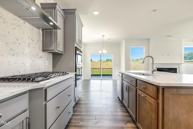 kitchen with tasteful backsplash, wall chimney exhaust hood, stainless steel appliances, sink, and an inviting chandelier