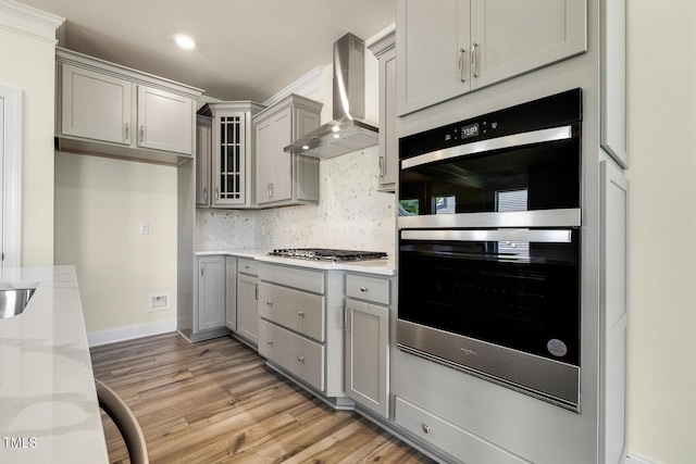 kitchen featuring gray cabinetry, wall chimney exhaust hood, light wood-type flooring, and stainless steel appliances