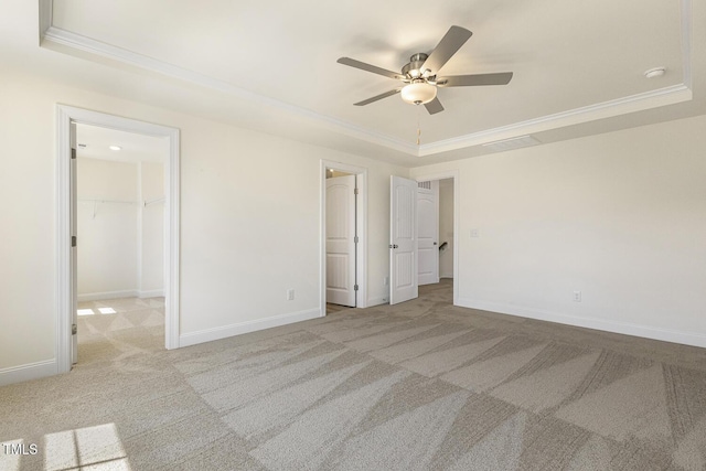 unfurnished bedroom featuring a walk in closet, a tray ceiling, ceiling fan, and light colored carpet