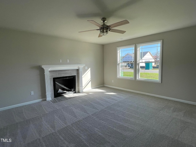 unfurnished living room with ceiling fan, a tile fireplace, and dark colored carpet