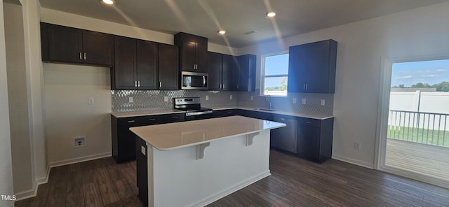 kitchen featuring a sink, appliances with stainless steel finishes, backsplash, a center island, and dark wood finished floors