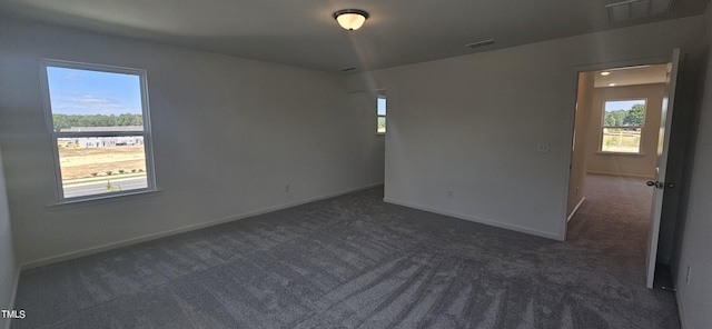 spare room with a wealth of natural light, dark carpet, and visible vents