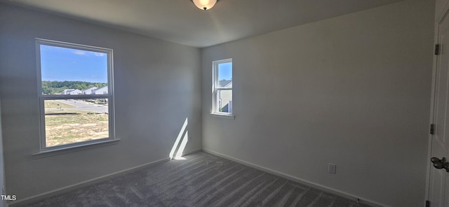 empty room with dark carpet, a wealth of natural light, and baseboards