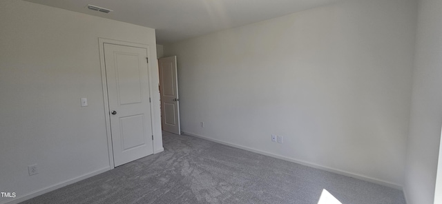 empty room with dark carpet, visible vents, and baseboards