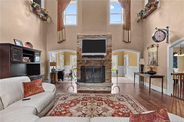 living room with a stone fireplace, dark hardwood / wood-style floors, a healthy amount of sunlight, and a towering ceiling