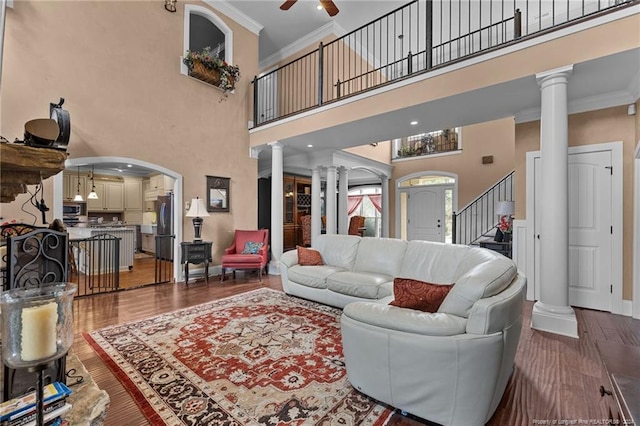 living room with a towering ceiling, ceiling fan, ornate columns, dark wood-type flooring, and ornamental molding