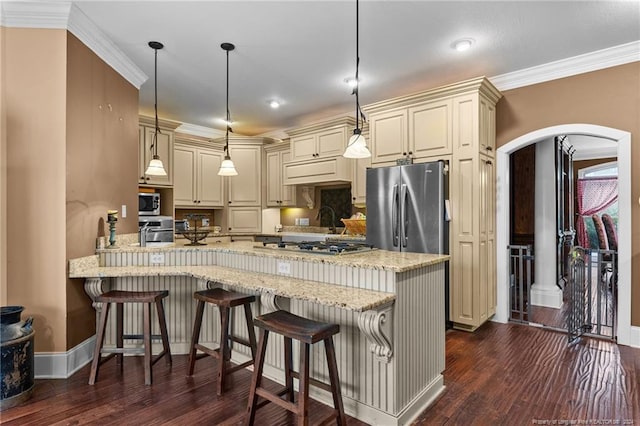 kitchen with appliances with stainless steel finishes, dark hardwood / wood-style floors, cream cabinets, and a breakfast bar