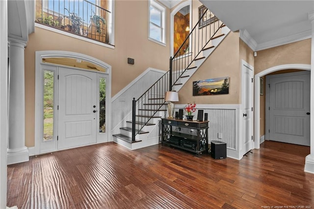 foyer entrance featuring ornamental molding, ornate columns, a towering ceiling, and dark wood-type flooring