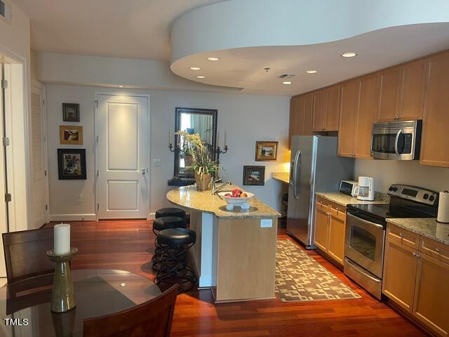 kitchen with light stone countertops, hardwood / wood-style floors, a kitchen island, and appliances with stainless steel finishes