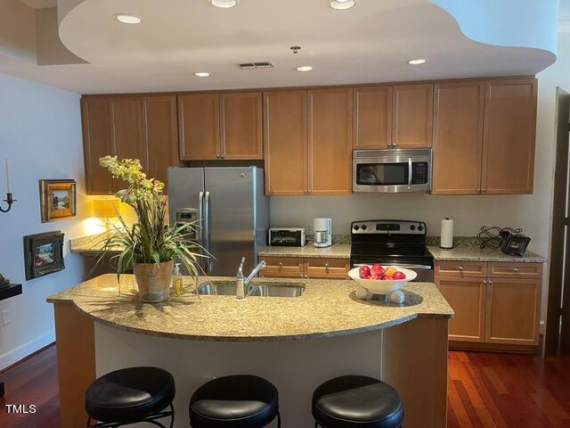 kitchen featuring dark hardwood / wood-style floors, stainless steel appliances, sink, and light stone countertops