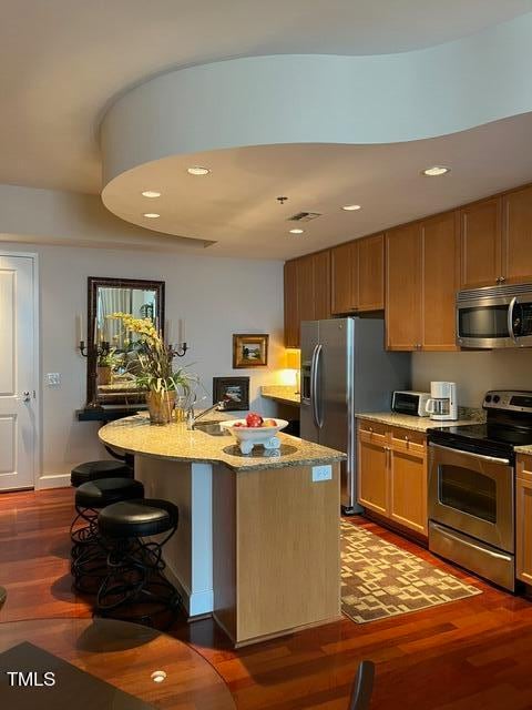 kitchen with light stone counters, a breakfast bar, stainless steel appliances, wood-type flooring, and a center island