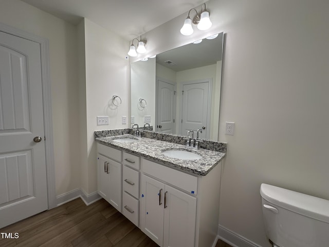 bathroom with double vanity, wood finished floors, a sink, and toilet