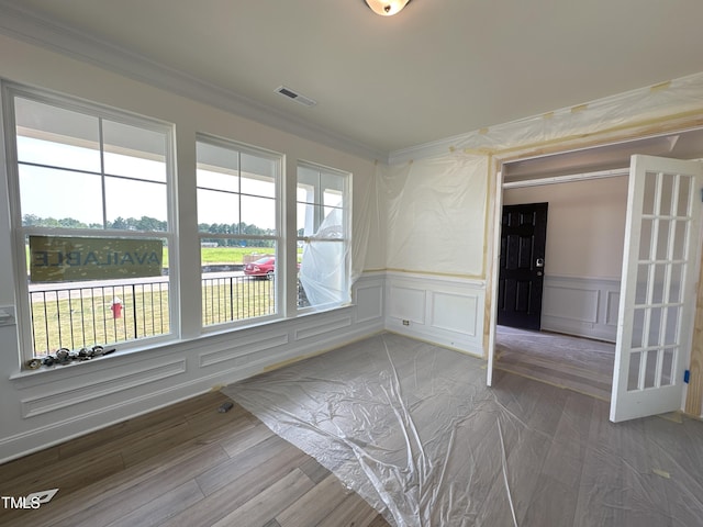 empty room featuring ornamental molding, wood finished floors, visible vents, and a decorative wall