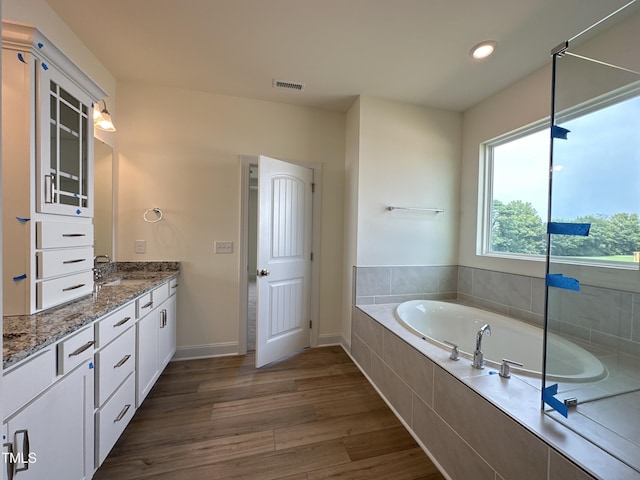 bathroom featuring wood finished floors, vanity, visible vents, baseboards, and a bath