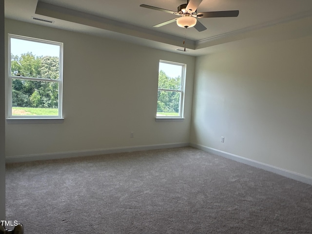 carpeted empty room with ceiling fan, baseboards, visible vents, and a raised ceiling