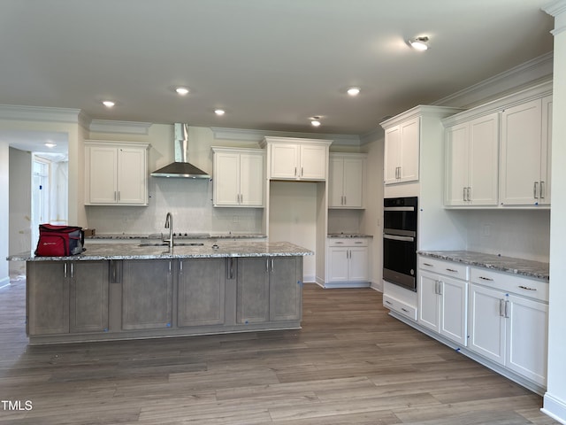 kitchen with wall chimney exhaust hood, a sink, white cabinets, and dobule oven black