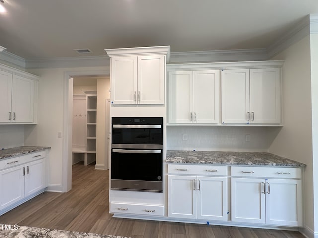 kitchen with light stone counters, double oven, ornamental molding, white cabinets, and wood finished floors