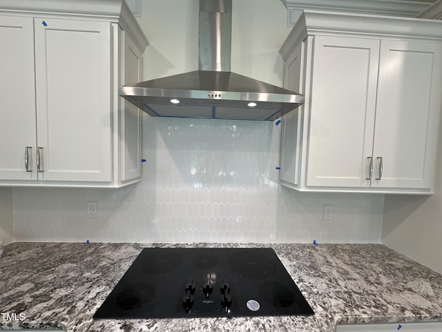 kitchen with white cabinets, wall chimney range hood, dark stone countertops, and black electric cooktop