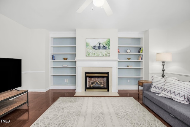 living room with ceiling fan, built in features, wood finished floors, and a fireplace with raised hearth