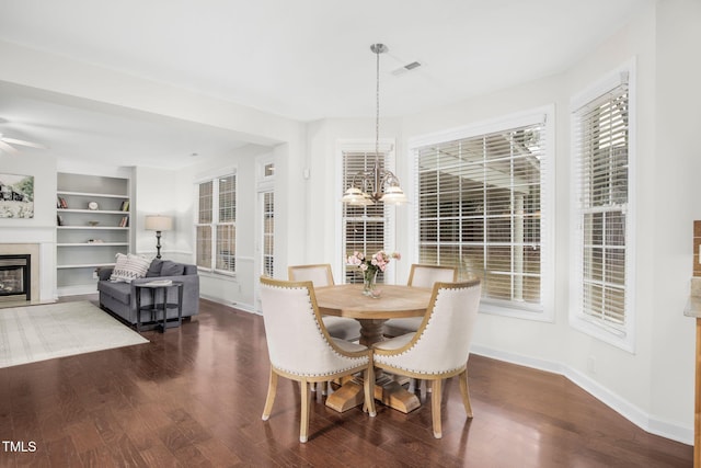 dining area featuring visible vents, built in shelves, wood finished floors, a glass covered fireplace, and baseboards