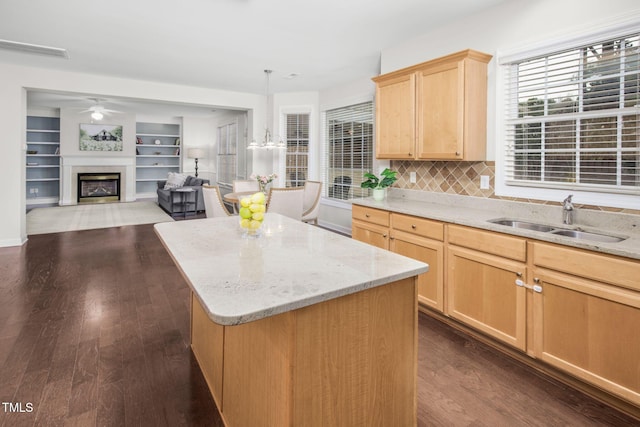 kitchen featuring a kitchen island, light brown cabinetry, dark wood finished floors, a glass covered fireplace, and a sink