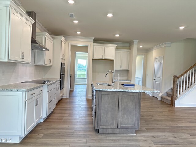 kitchen featuring white cabinets, a sink, wall chimney exhaust hood, and black appliances