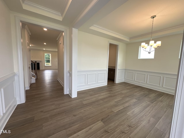 empty room with ornamental molding, a tray ceiling, dark wood-type flooring, and a chandelier