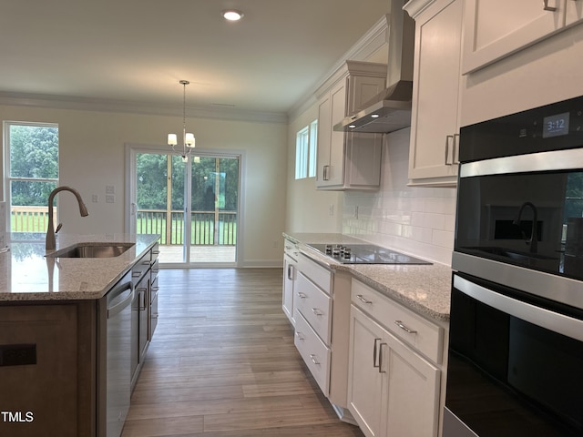 kitchen featuring decorative backsplash, wall chimney exhaust hood, appliances with stainless steel finishes, ornamental molding, and a sink