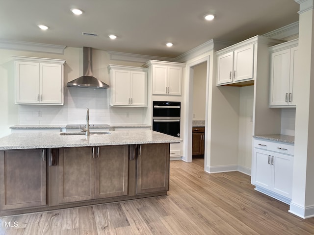 kitchen with dobule oven black, wall chimney exhaust hood, and white cabinets