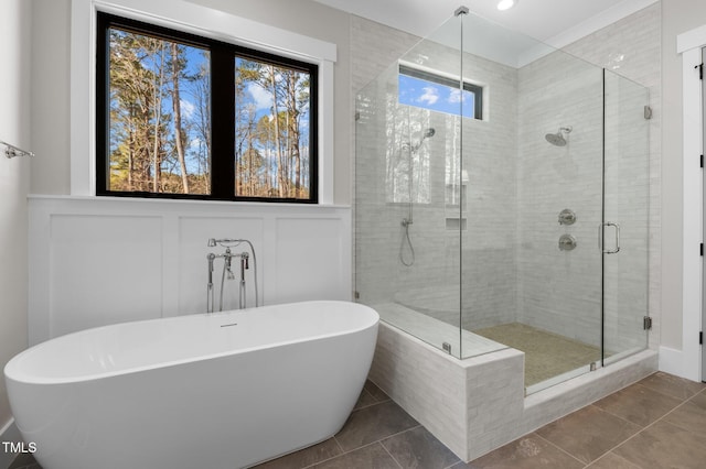 full bath featuring a soaking tub, a decorative wall, a stall shower, wainscoting, and tile patterned floors