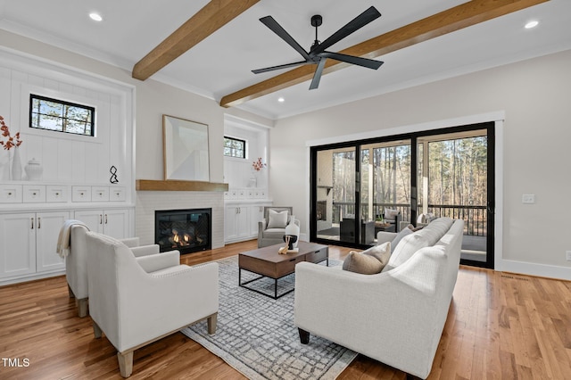 living room featuring light wood-style floors, plenty of natural light, a brick fireplace, and beamed ceiling