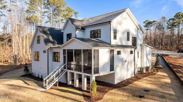 rear view of property featuring a sunroom, roof with shingles, and stairs