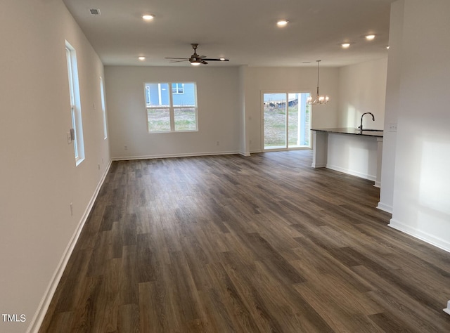 unfurnished living room with ceiling fan with notable chandelier, dark wood-type flooring, and a healthy amount of sunlight