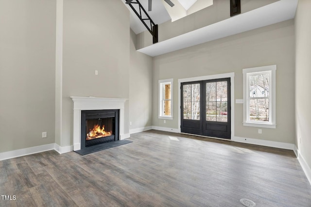 unfurnished living room with a high ceiling, plenty of natural light, french doors, and wood-type flooring