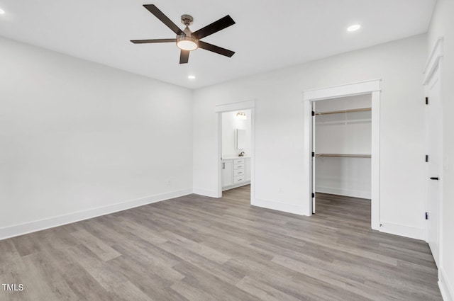 unfurnished bedroom featuring ceiling fan, a closet, hardwood / wood-style floors, ensuite bathroom, and a walk in closet