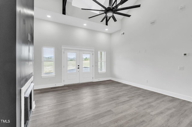 unfurnished living room with ceiling fan, a towering ceiling, french doors, and wood-type flooring