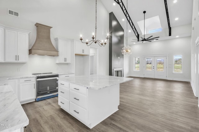 kitchen with a kitchen island, hardwood / wood-style flooring, range with electric stovetop, custom exhaust hood, and a high ceiling