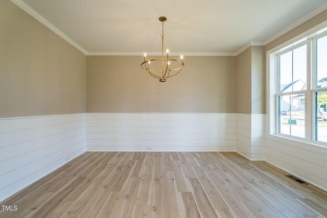 spare room with visible vents, light wood-style flooring, ornamental molding, wainscoting, and a chandelier