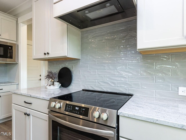 kitchen with light stone countertops, tasteful backsplash, range hood, and appliances with stainless steel finishes