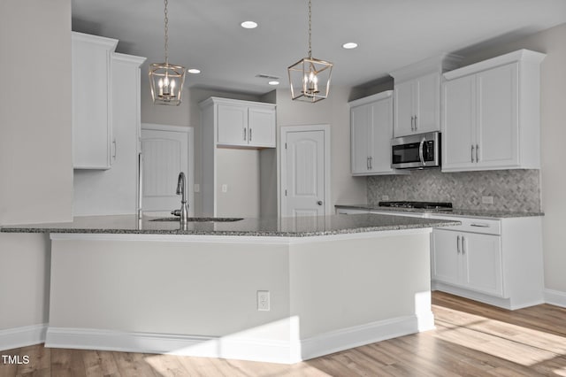 kitchen with white cabinets, light wood-type flooring, hanging light fixtures, and stone counters