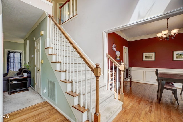 staircase featuring a notable chandelier, a textured ceiling, ornamental molding, and light colored carpet