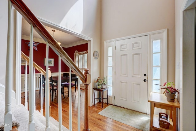 entrance foyer featuring ornamental molding, a towering ceiling, and light wood-type flooring