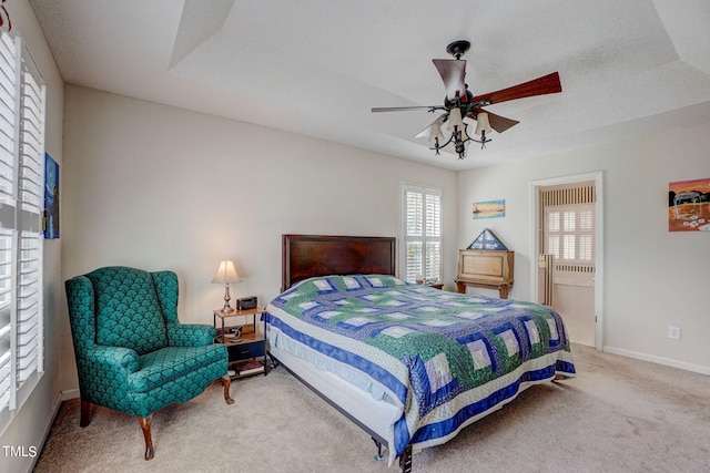 carpeted bedroom with ceiling fan, ensuite bath, and a tray ceiling