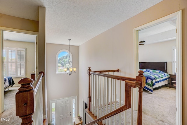 hallway featuring an inviting chandelier, a textured ceiling, and light colored carpet