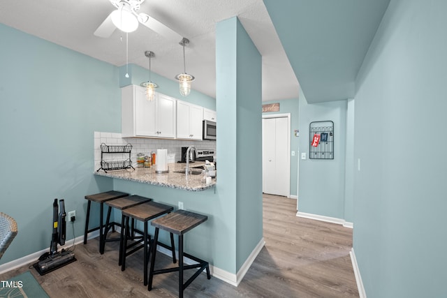 kitchen featuring white cabinets, tasteful backsplash, decorative light fixtures, light hardwood / wood-style flooring, and a breakfast bar area