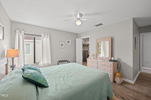 bedroom featuring ceiling fan, wood-type flooring, a textured ceiling, a walk in closet, and a closet