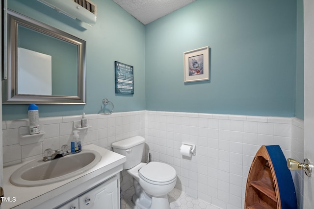 bathroom with vanity, tile walls, tile patterned flooring, toilet, and a textured ceiling