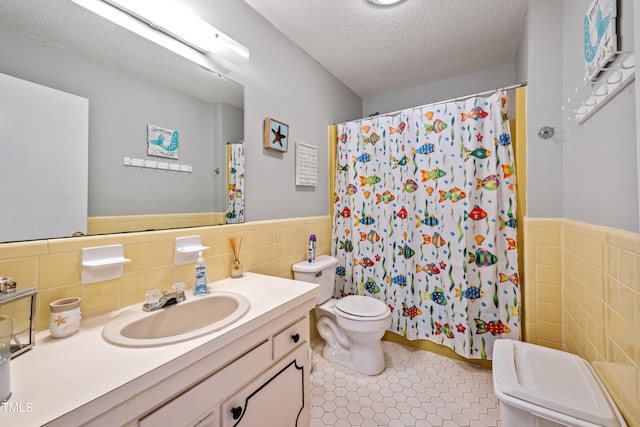 bathroom featuring tile patterned flooring, toilet, tile walls, vanity, and a textured ceiling