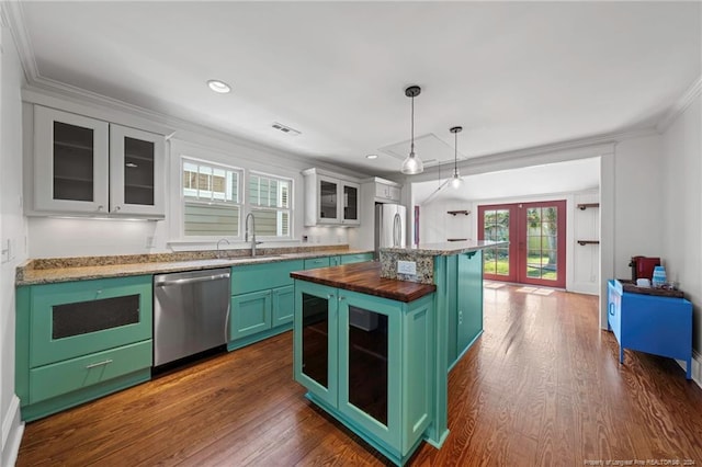 kitchen with appliances with stainless steel finishes, white cabinets, a kitchen island, butcher block counters, and pendant lighting