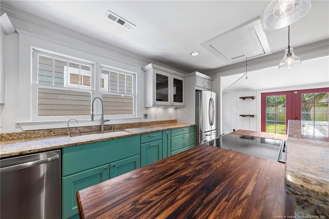 kitchen with green cabinetry, decorative light fixtures, sink, stainless steel appliances, and dark stone countertops